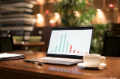 open laptop with vertical bargraph on screen, coffee in ceramic cup, on dark wood desk