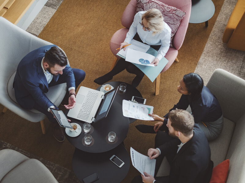 view from above of 4 business people, 2 men, 2 women, working around an oblong coffee table