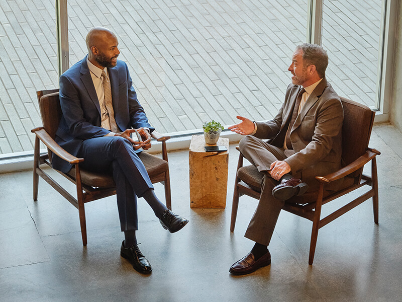 two businessmen seated in modern office chairs talking
